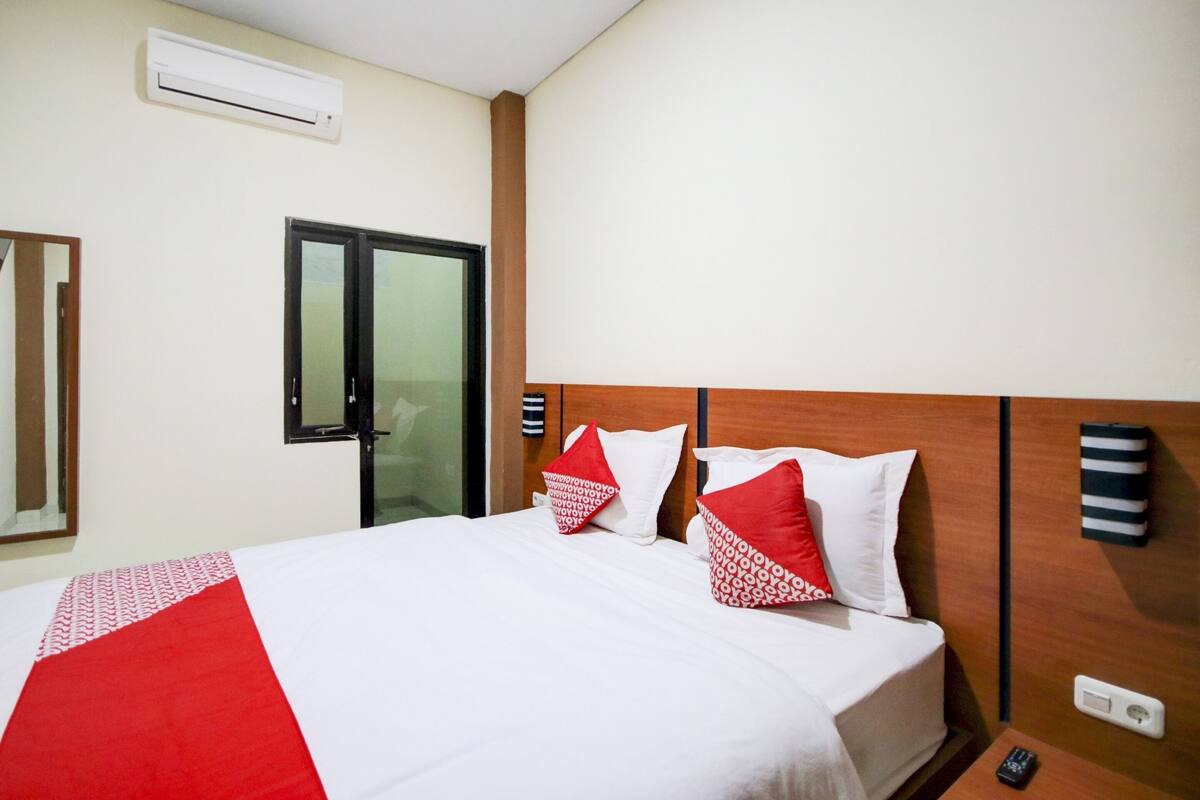 A hotel room with a bed, a mirror, a door, and a wall-mounted air conditioner.