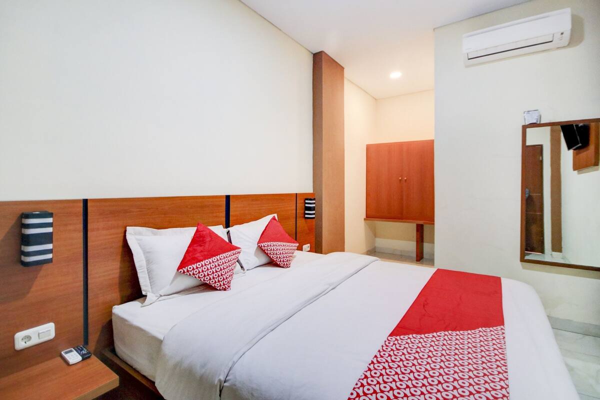 A hotel room with a bed, a bedside table, a mirror, and a wardrobe.