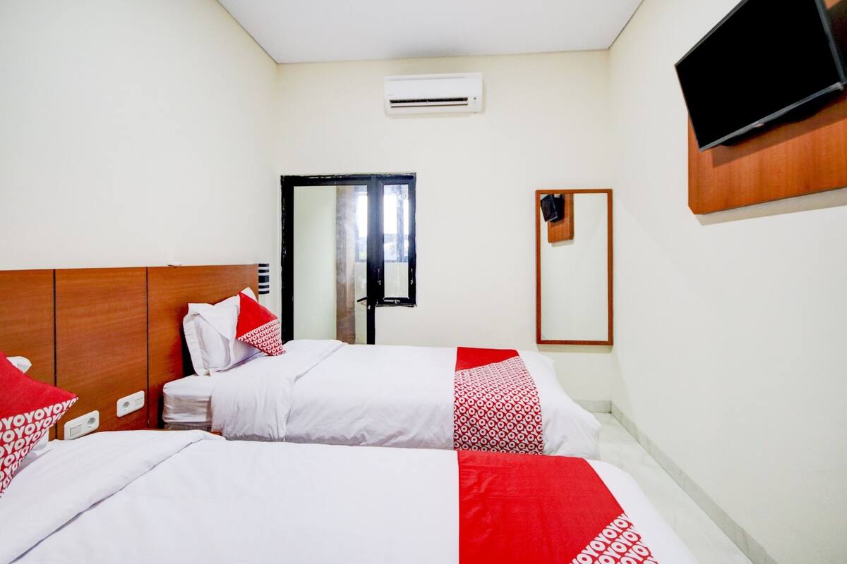 A hotel room with two beds, a TV mounted on the wall, an air conditioning unit, and a mirror.