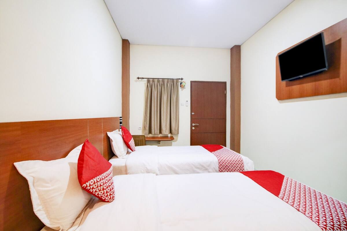 A hotel room with two beds, a television mounted on the wall, a door, and a window with curtains.
