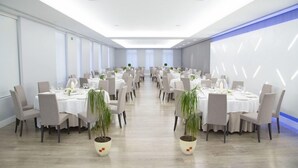 A large, well-lit conference room with multiple round tables, each set with white tablecloths, chairs, and potted plants. - Mendez Nunez (Lugo)