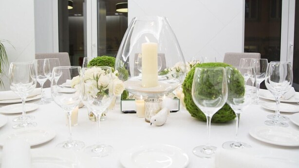 A table set for a formal event with clear glassware, white plates, and a centerpiece featuring a candle and decorative items. - Mendez Nunez (Lugo)