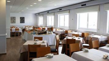 A dining area with tables set for service, large windows, and artwork on the walls.