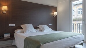 A modern hotel room with a large bed, a green throw blanket, wooden flooring, and a unique geometric pendant light. - Mendez Nunez (Lugo)