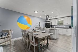 Une cuisine moderne avec des meubles blancs, un grand îlot central et un coin repas comprenant une table et des chaises en bois.