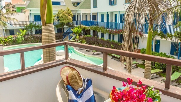 Un balcon donnant sur une piscine, une chaise, un sac en osier et un panier de fleurs.