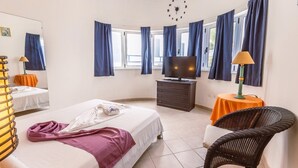Une chambre d’hôtel avec un lit, une télévision, une commode, une chaise et une fenêtre avec des rideaux.