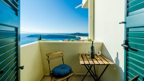 A balcony with a view of the sea, a wooden chair, a small table with a bottle and glass, and a window with shutters. - Sun City Apartment (Dubrovnik)
