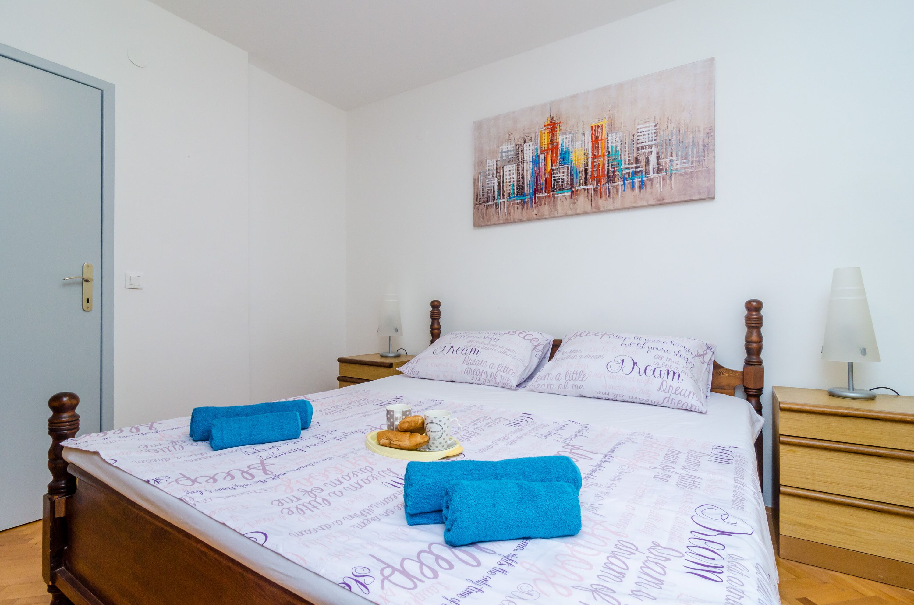 A neatly made bed with blue towels, a plate of pastries, and a pillow with 'Dream' printed on it.
