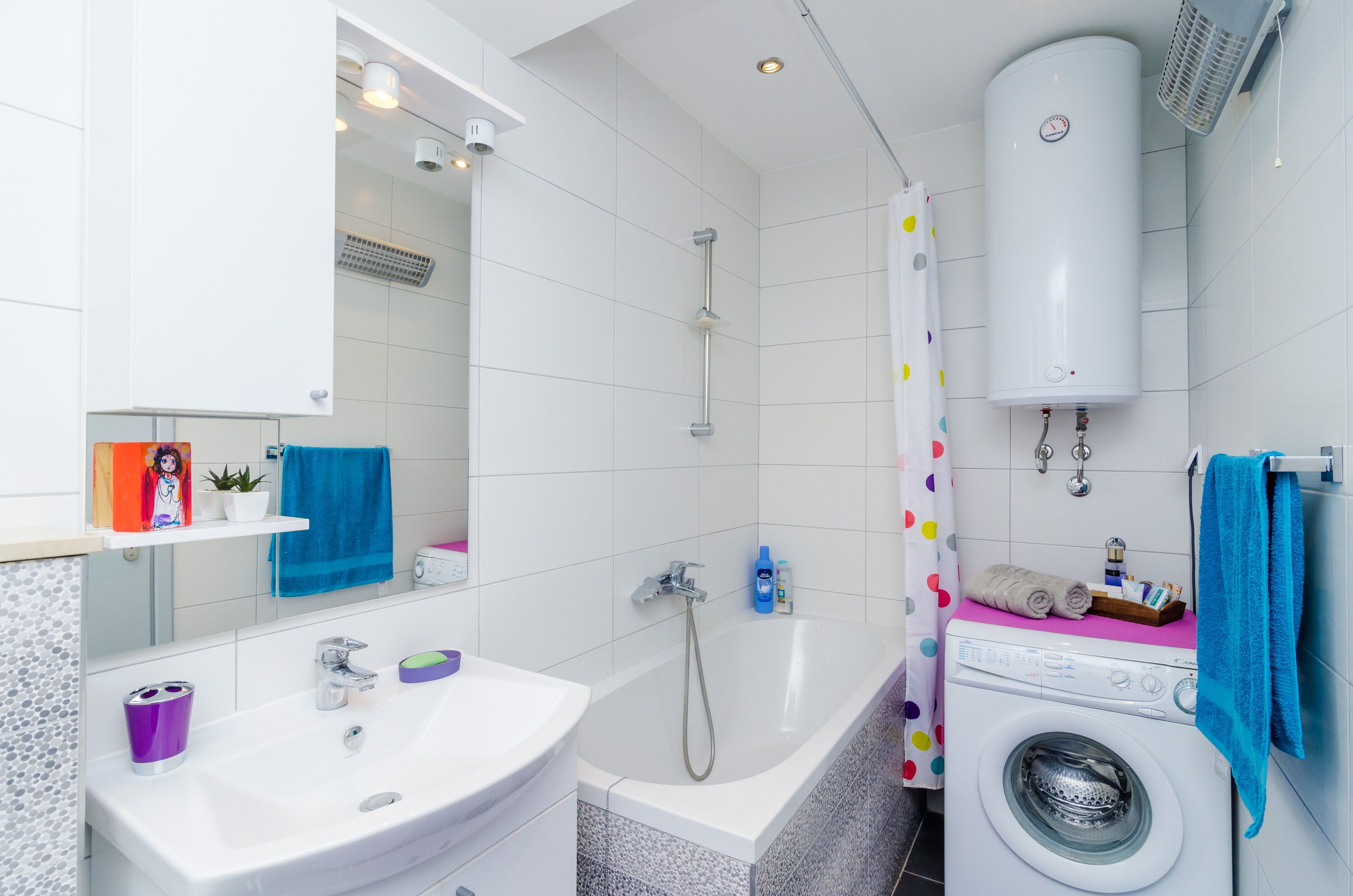 A modern bathroom with a white sink, mirror, shower, and a built-in washing machine.