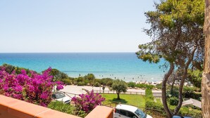 A coastal view with a beach, parked cars, and vibrant pink flowers. - Fantastic Seaview Turquoise House (Santa Margherita di Pula)