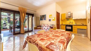 A modern hotel room with a large bed, a dining area, and a kitchen. - Yellow House with garden, 130 meters from the beach (Santa Margherita di Pula)
