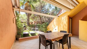 A patio with a table and chairs, a view of a garden, and a building in the background. - Yellow House with garden, 130 meters from the beach (Santa Margherita di Pula)