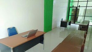 Ein Zimmer mit Schreibtisch, Stuhl und Laptop. Man sieht eine grüne Säule und ein Fenster mit Blick.