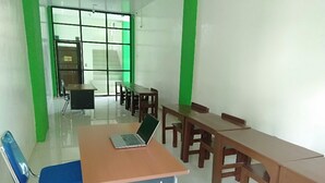 Ein Klassenzimmer mit einem Laptop auf einem Schreibtisch, Holztischen und -stühlen.
