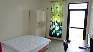 Ein Zimmer mit einem Bett, einem Schreibtisch, einem Stuhl, einem Kleiderschrank und einem Fenster mit Vorhang.