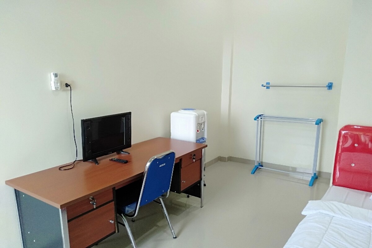 Ein Zimmer mit Schreibtisch, Stuhl, Bett und Heizkörper.