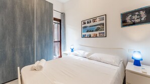 A modern bedroom with a large bed, a nightstand with a lamp, and a wall-mounted picture. - Blue House, 300 meters from the beach (Santa Margherita di Pula)
