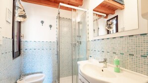 A bathroom with a glass shower enclosure, a bidet, a sink with a mirror, and a tiled backsplash. - Blue House, 300 meters from the beach (Santa Margherita di Pula)