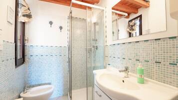 Un bagno con cabina doccia in vetro, un bidet, un lavandino con specchio e schienale piastrellato.