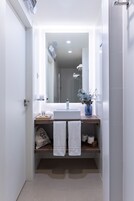 Un baño moderno con lavamanos, espejo y toallero blancos.