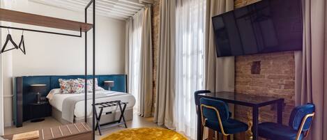 A modern hotel room with a bed, a desk, a TV, and a dining area.