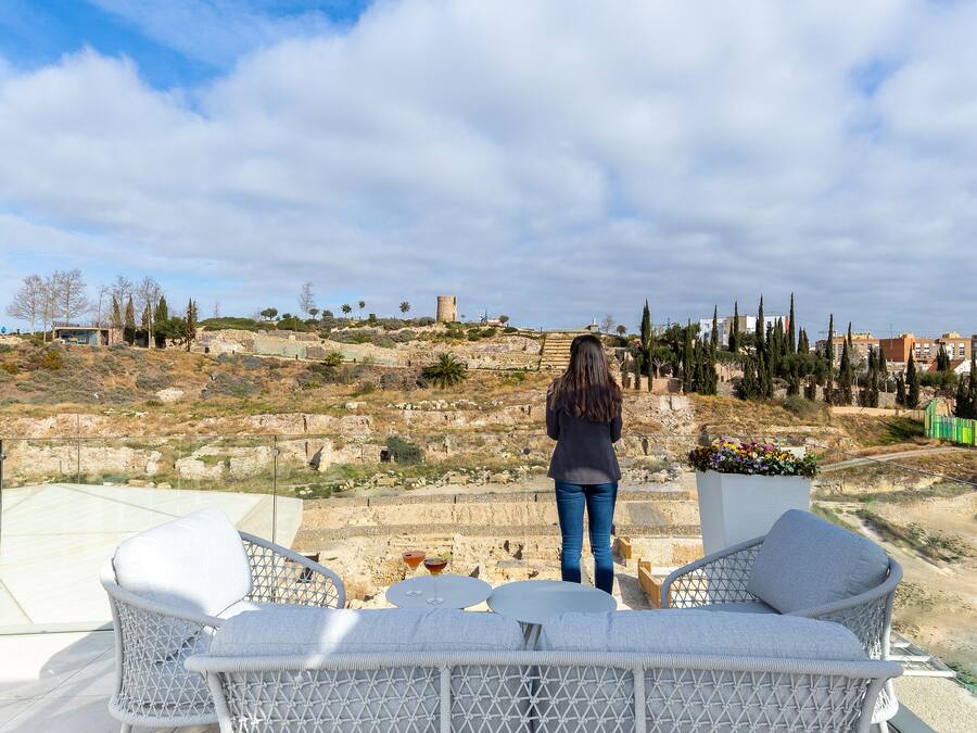 Una terrazza con mobili in vimini bianco, vista panoramica sul paesaggio circostante e una persona in lontananza.