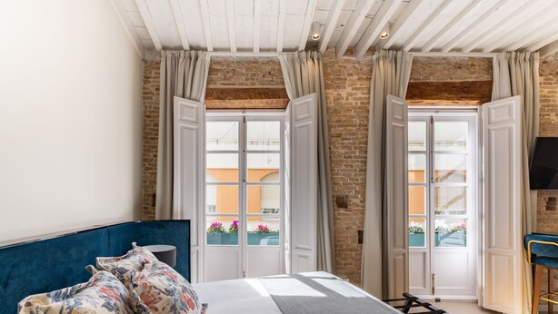 A bedroom with a bed, curtains, a TV, and a view of the outside. - La Casa de las Flores  (Cartagena)