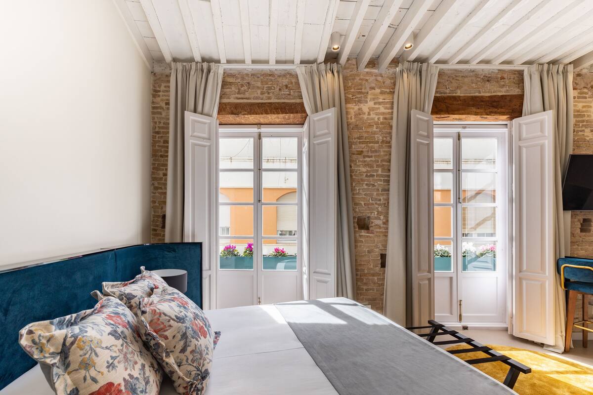 A bedroom with a bed, curtains, a TV, and a view of the outside.