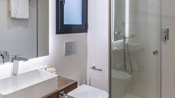Un baño moderno con un espejo grande, cabina de ducha de vidrio y tocador de madera.