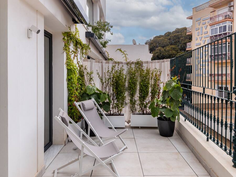 A balcony with white lounge chairs, potted plants, and a green metal railing.