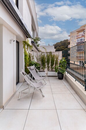 A balcony with white lounge chairs, potted plants, and a green metal railing. - La Casa de las Flores  (Cartagena)