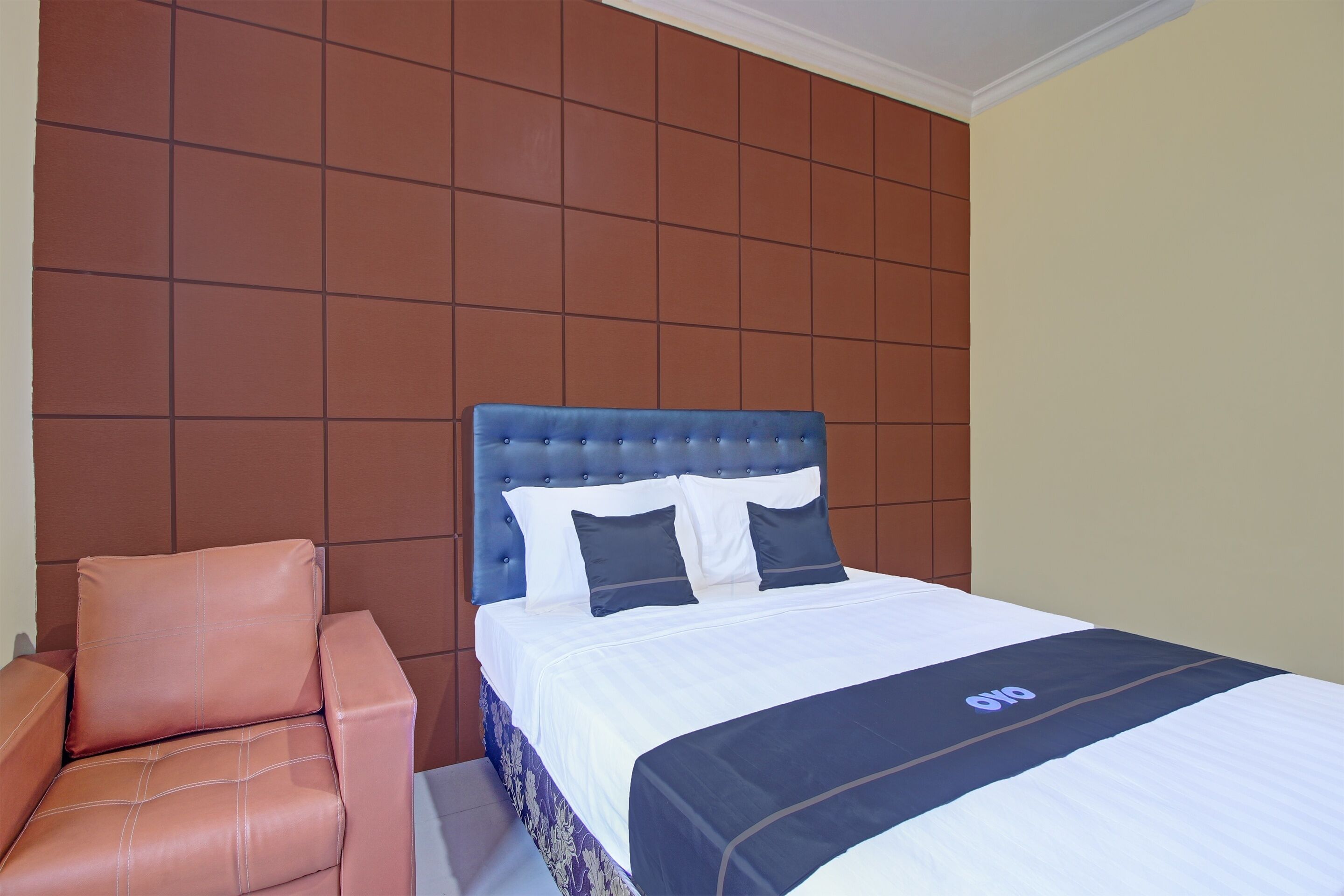 A hotel room with a bed, a headboard, and a chair.