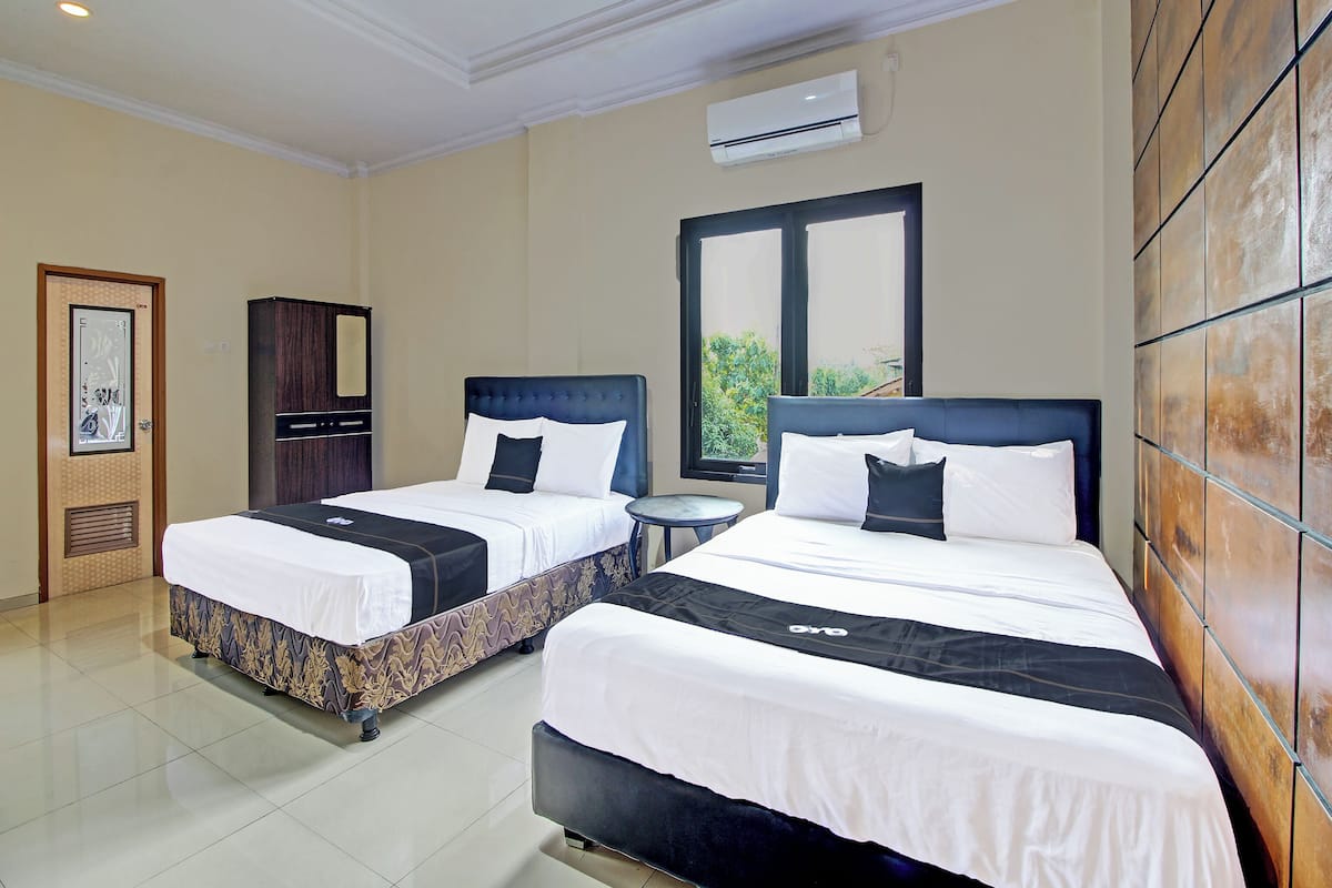 A hotel room with two beds, an air conditioning unit, a window, and a door.