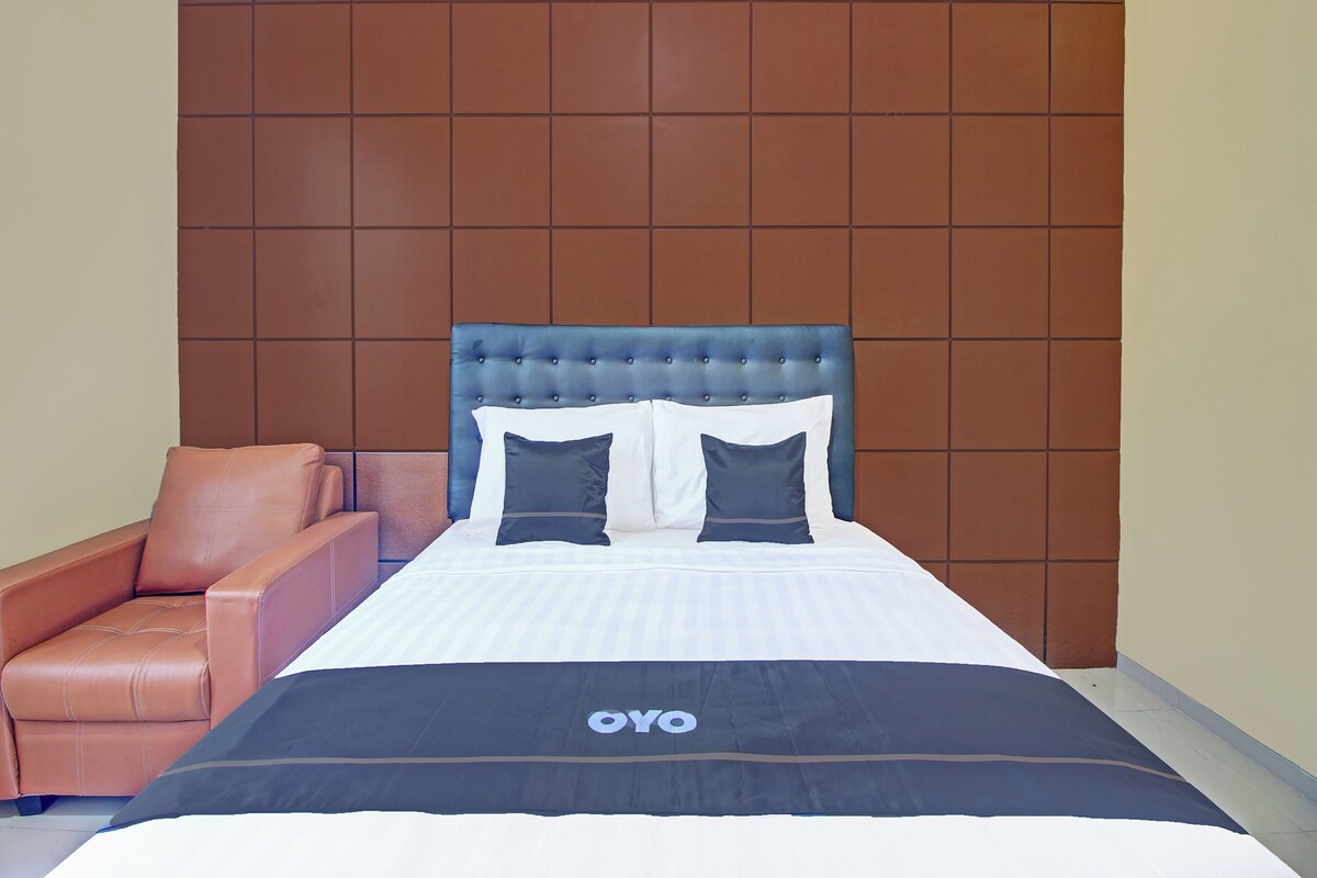 A hotel room with a bed, a brown leather chair, and a wall with a grid pattern.
