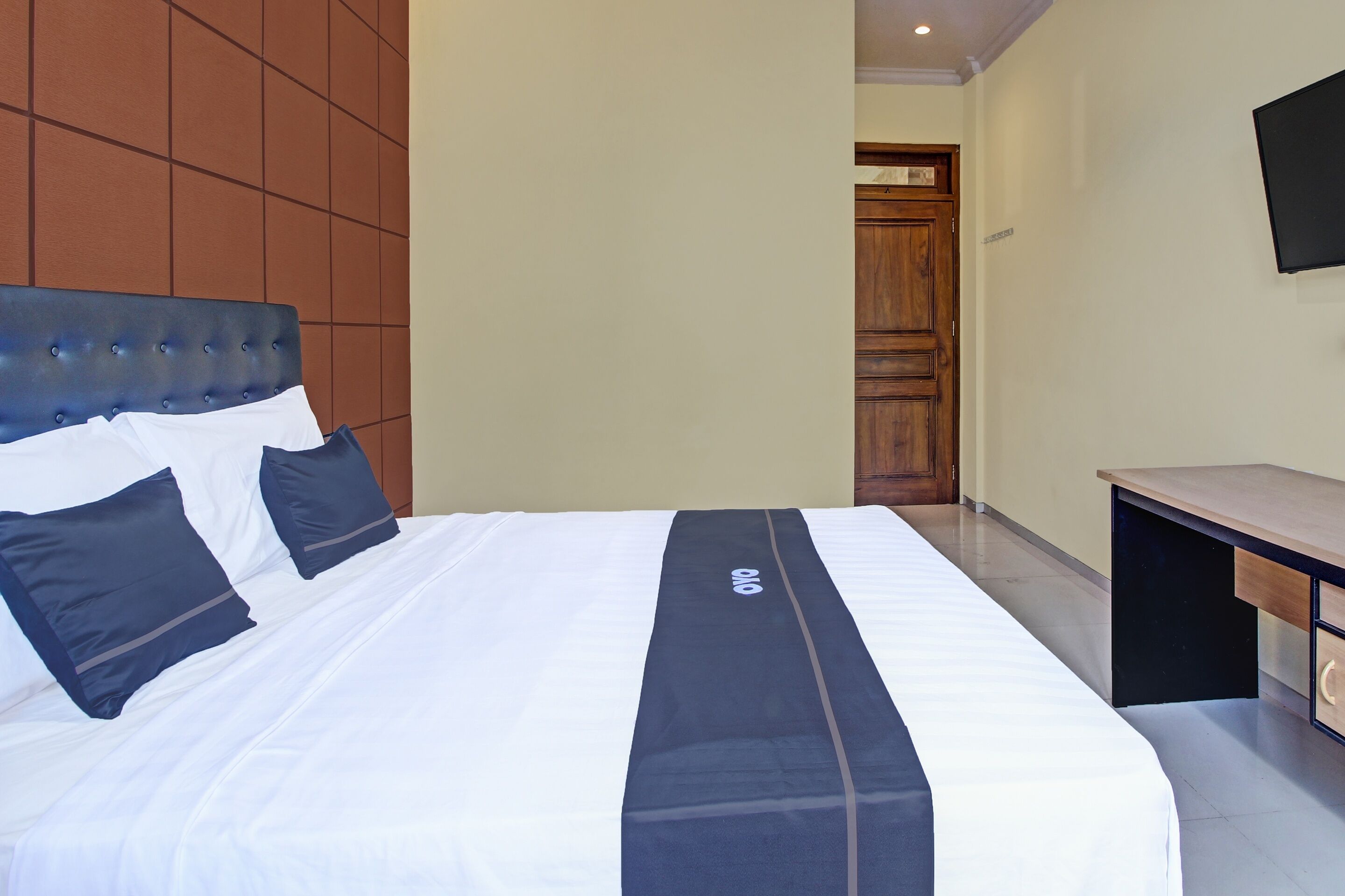 Una habitación de hotel con una cama grande, cabecera de madera, un escritorio y televisión en la pared.