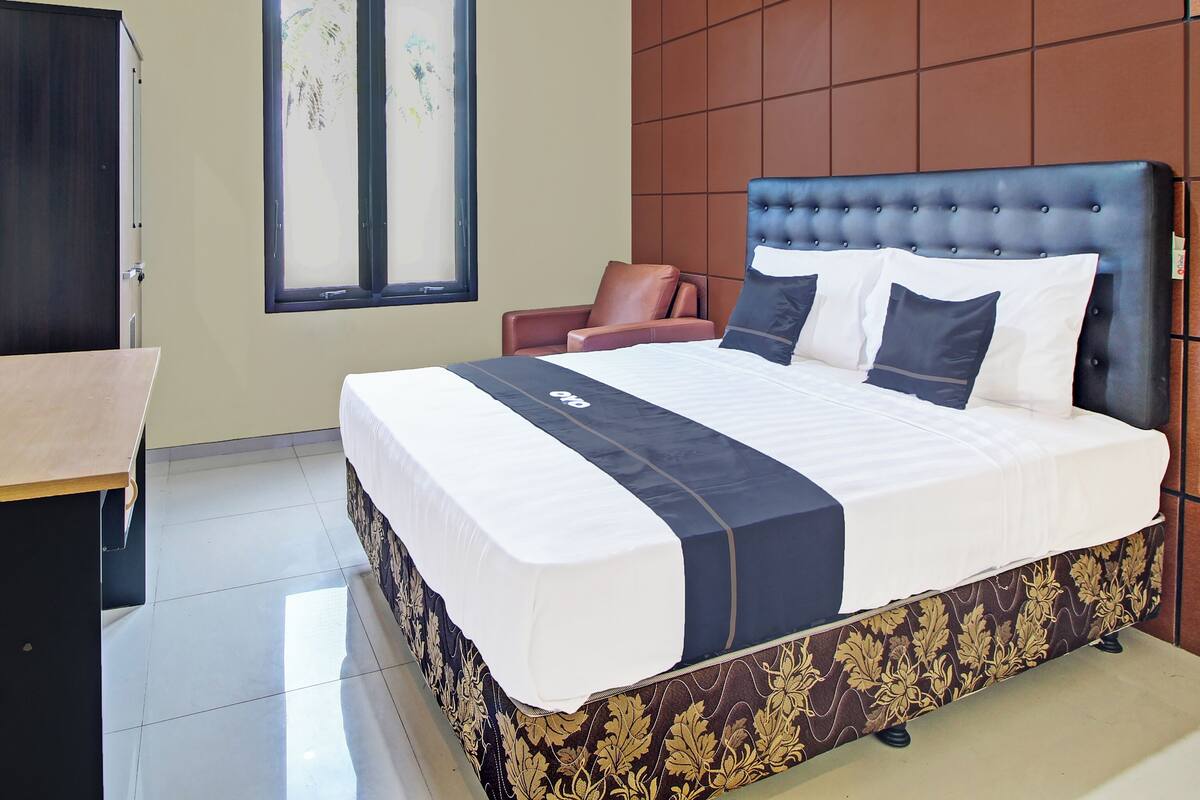 A hotel room with a large bed, a desk, a chair, a window, and a wall-mounted air conditioner.
