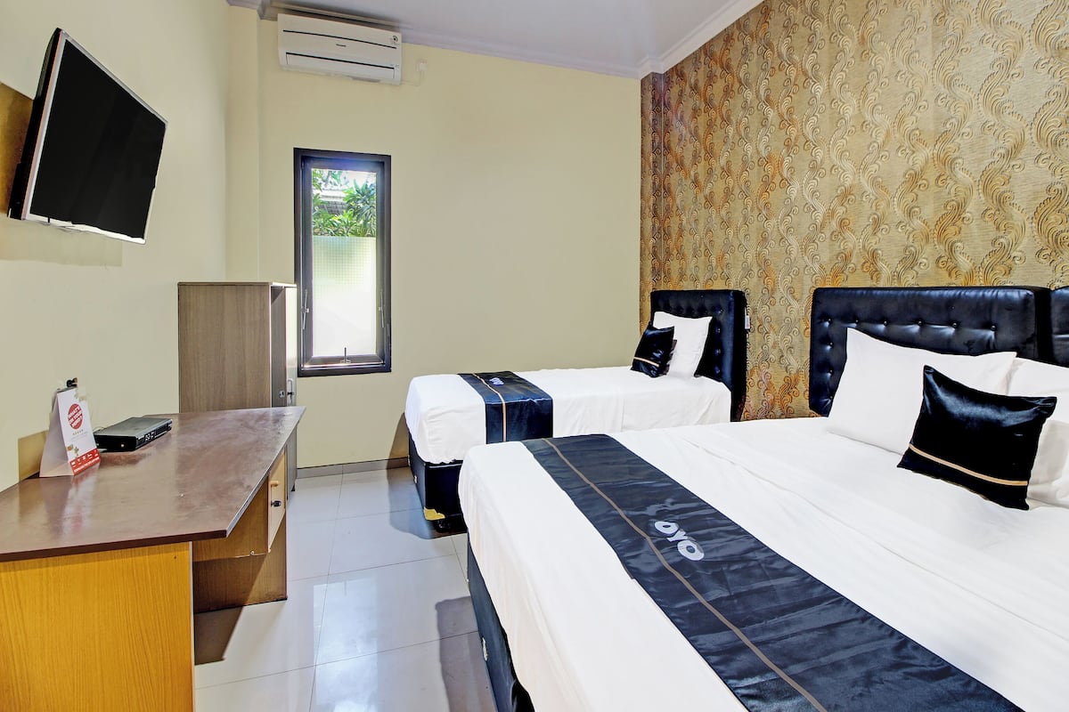A hotel room with two beds, a desk, a TV, and a window.