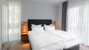 A modern hotel room with two beds, a wooden headboard, and a large window with sheer curtains. - Sporthotel Neuruppin - Apartmenthaus mit Ferienwohnungen (Neuruppin)