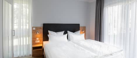 A modern hotel room with two beds, a wooden headboard, and a large window with sheer curtains.