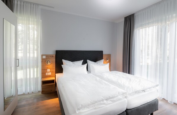 A modern hotel room with two beds, a wooden headboard, and a large window with sheer curtains.