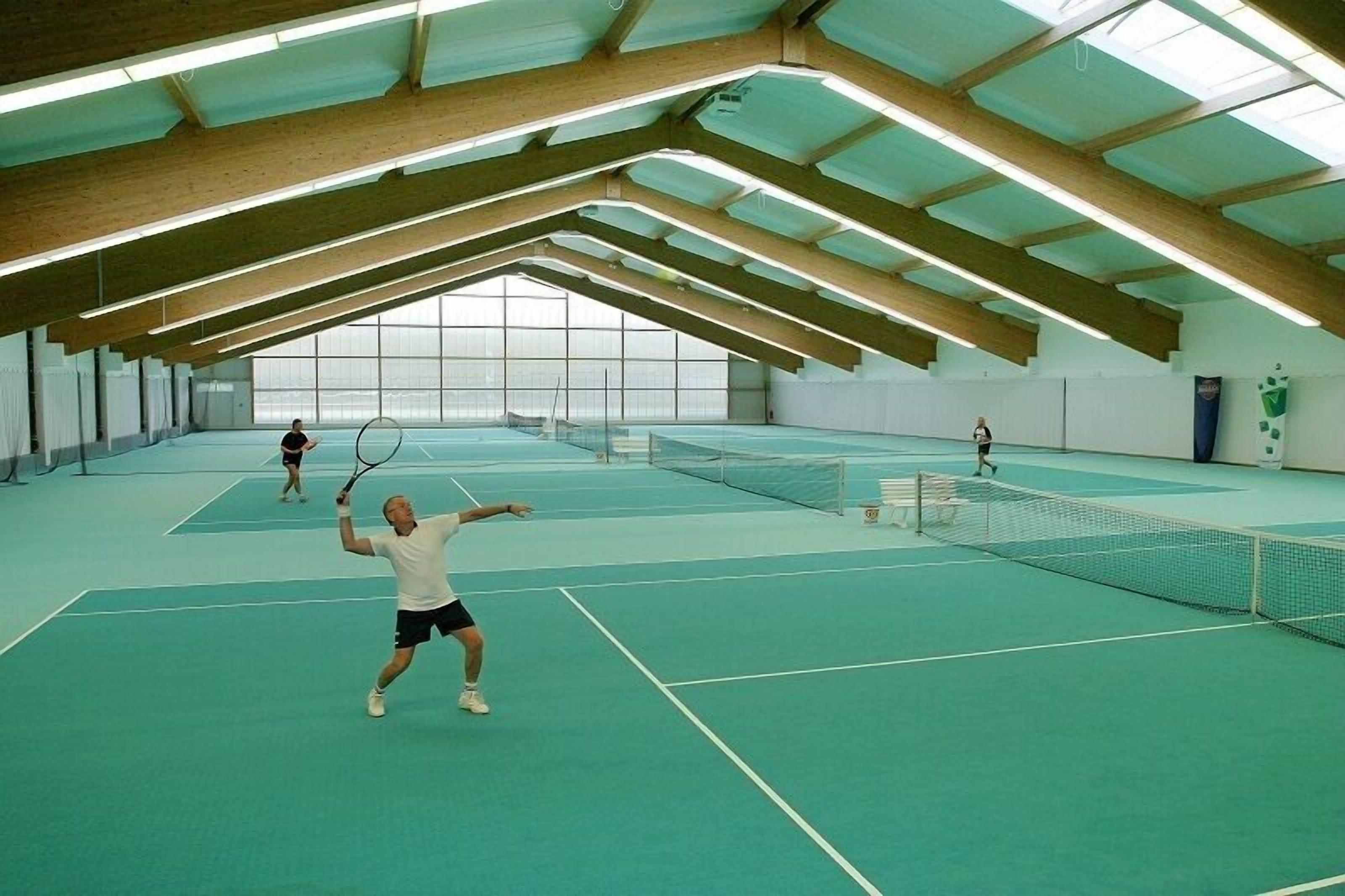 An indoor tennis court with a high ceiling and skylights.