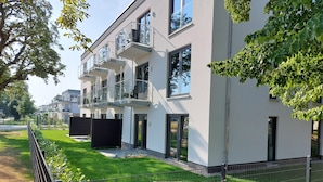 A modern multi-story residential building with balconies, a well-maintained lawn, and a metal fence. - Sporthotel Neuruppin - Apartmenthaus mit Ferienwohnungen (Neuruppin)