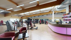 A spacious gym with various exercise machines, a reception desk, and a wooden ceiling. - Sporthotel Neuruppin - Apartmenthaus mit Ferienwohnungen (Neuruppin)