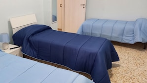 Una habitación con dos camas, cada una con colcha azul, una mesita de noche con lámpara y un armario de madera.