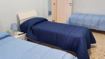 Ein Zimmer mit zwei Betten, jeweils mit blauer Bettdecke, einem Nachttisch mit Lampe und einem Holzschrank.