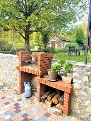 Una barbacoa de maó amb una paret de pedra, una planta en test i un regador.