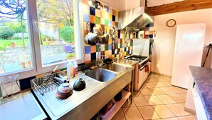 Una cocina con un ventanal grande, salpicadero de azulejos, electrodomésticos de acero inoxidable y techo de madera.