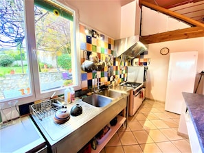 A kitchen with a large window, a tiled backsplash, stainless steel appliances, and a wooden ceiling.