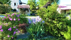 Una casa de piedra con techo de tejas, rodeada de exuberante vegetación y plantas en flor.